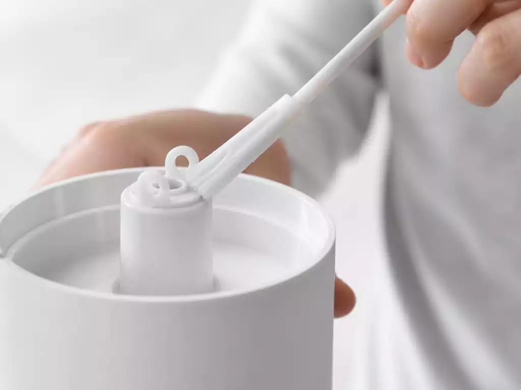 Person cleaning a humidifier nozzle with a small brush