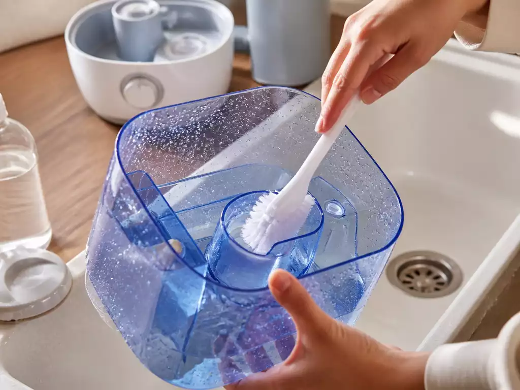 Person cleaning a humidifier tank with a brush and cleaning solution, showing clean water and sparkling interior