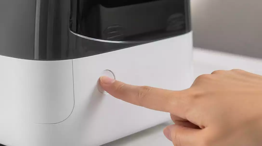 Hand pressing a reset button on a Boneco humidifier, close-up, clean background